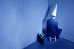 businessman-sitting-in-corner-with-dunce-hat
